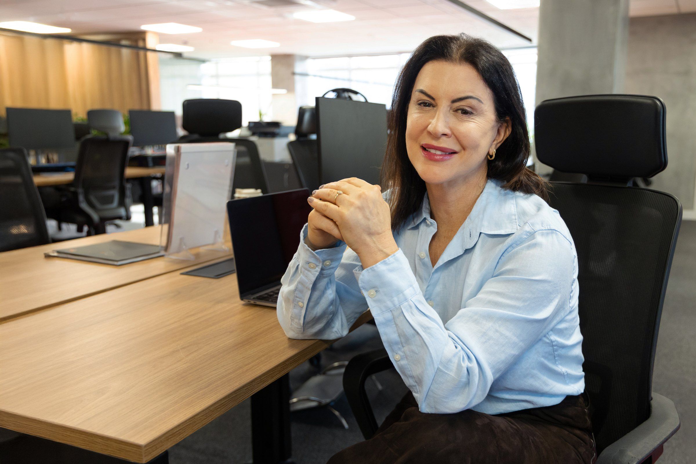 Raquel Araújo sentada em um escritório aberto, sorrindo
