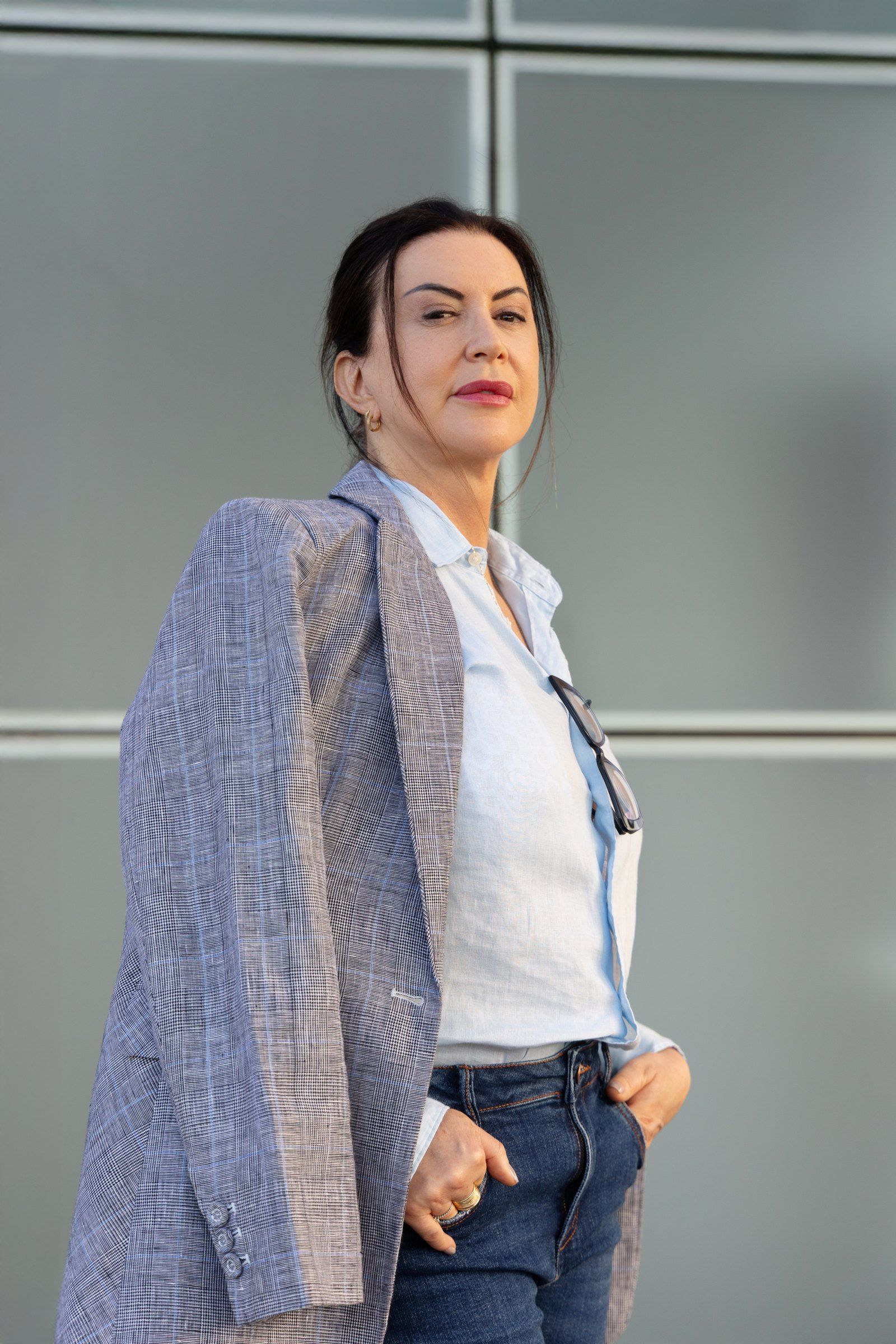 Raquel Araújo em pé, de blazer, em frente a uma parede de vidro