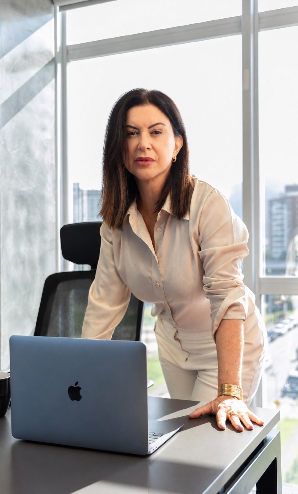 Raquel Araújo em seu escritório, apoiada na mesa de trabalho
